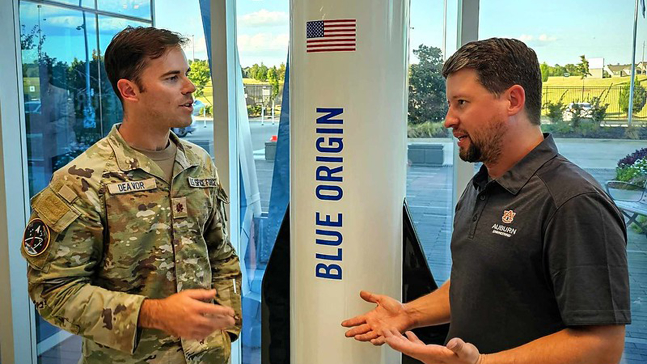 two men talking, rocket with blue origin written on it, American flag