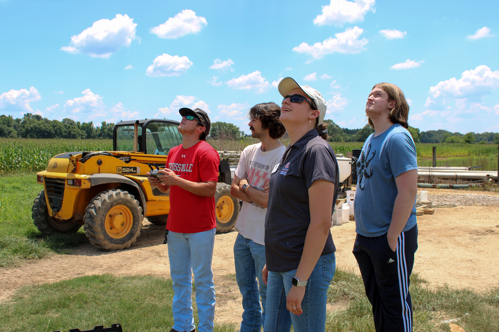 group of students and instructor looking up at the sky while flying a drone