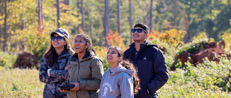 Students grouped around a drone pilot watching the drone fly