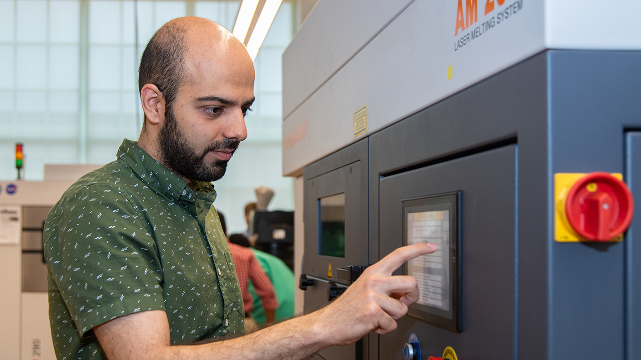 A researcher in the National Center for Additive Manufacturing Excellence is pictured operating an additive manufacturing machine.