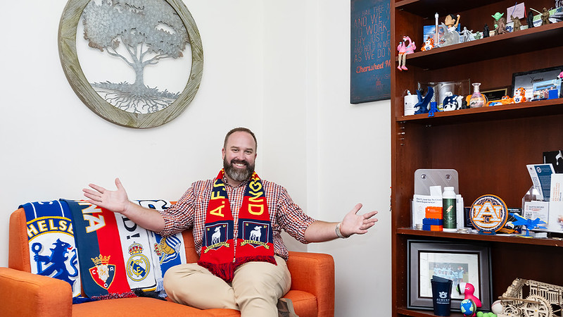 A student uses a driving simulator in a laboratory, seated at a steering wheel with multiple screens displaying a simulated roadway.