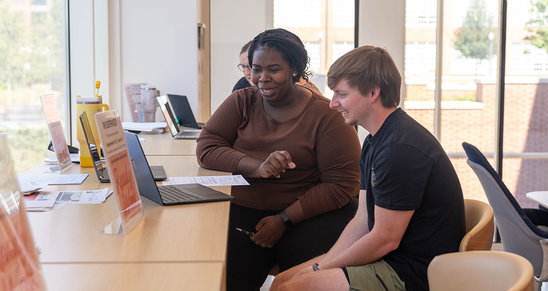 A career coach and Auburn Engineering student sit together at a counter reviewing materials on a laptop.