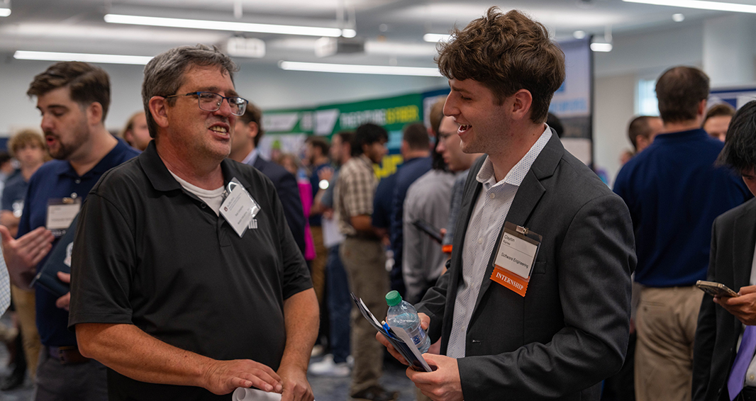 An Auburn Engineering student wearing a suit speaks with an employer representative during a crowded career fair.