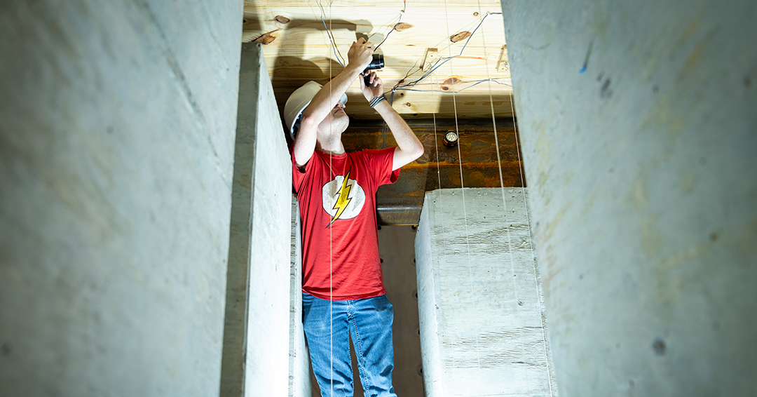A graduate student installs sensors and wiring beneath a timber test specimen in Auburn’s Advanced Structural Engineering Laboratory.