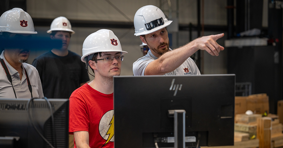 David Roueche points toward structural testing equipment while working with a graduate student in Auburn’s Advanced Structural Engineering Laboratory.