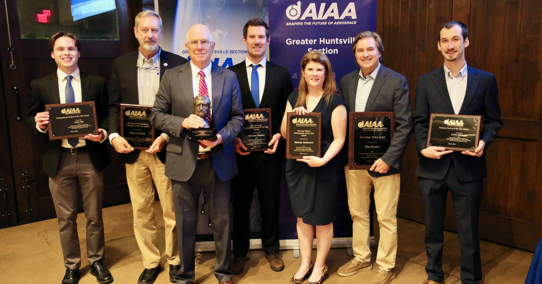 Seven Auburn aerospace engineering students and alumni stand together holding AIAA awards in front of a Greater Huntsville Section banner.
