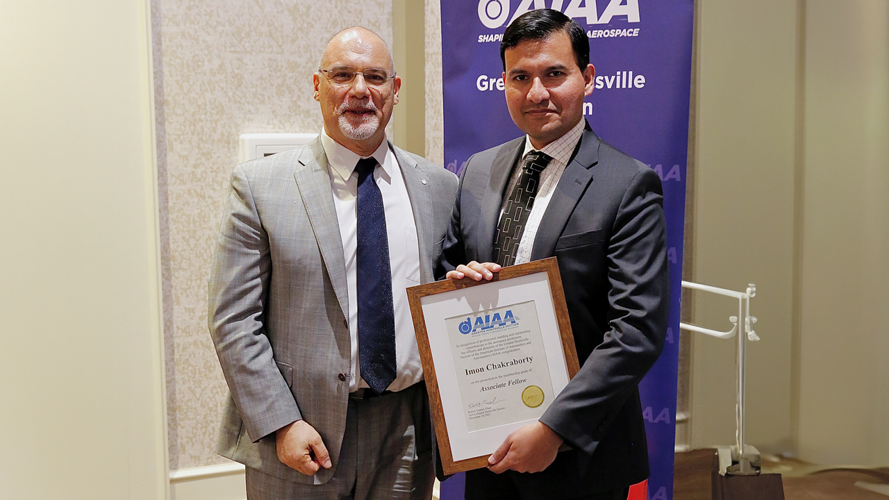 two men poses for photo with one man holding award.