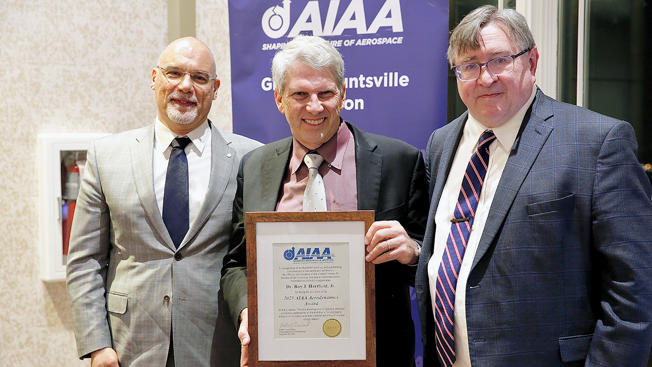 two men poses for photo with one man holding award.