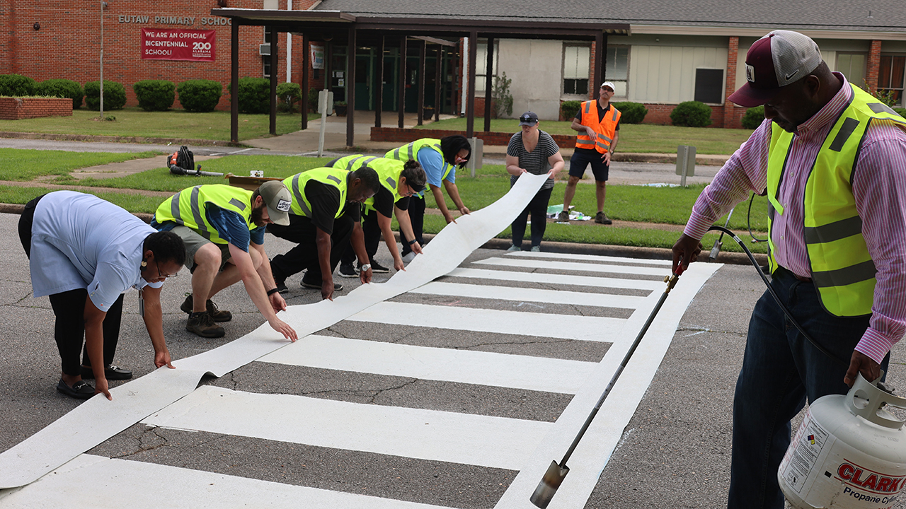 Several people laying down white lines to form a crosswalk.