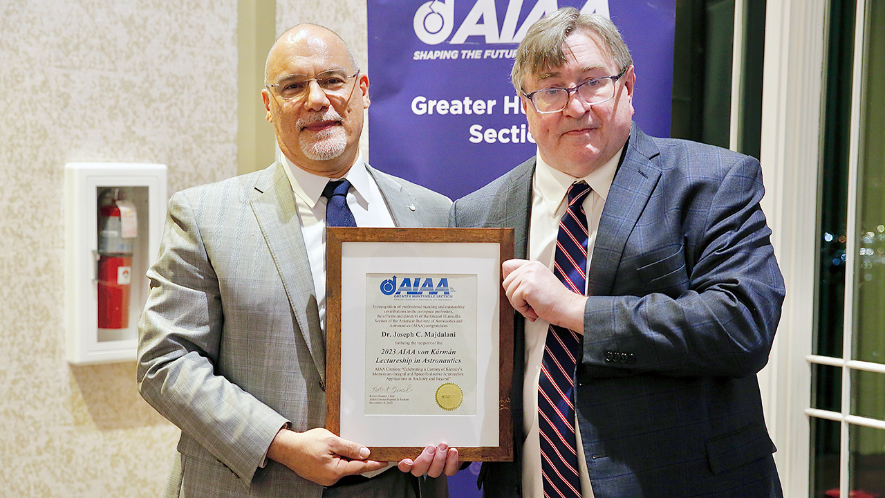  two men poses for photo with one man holding award.