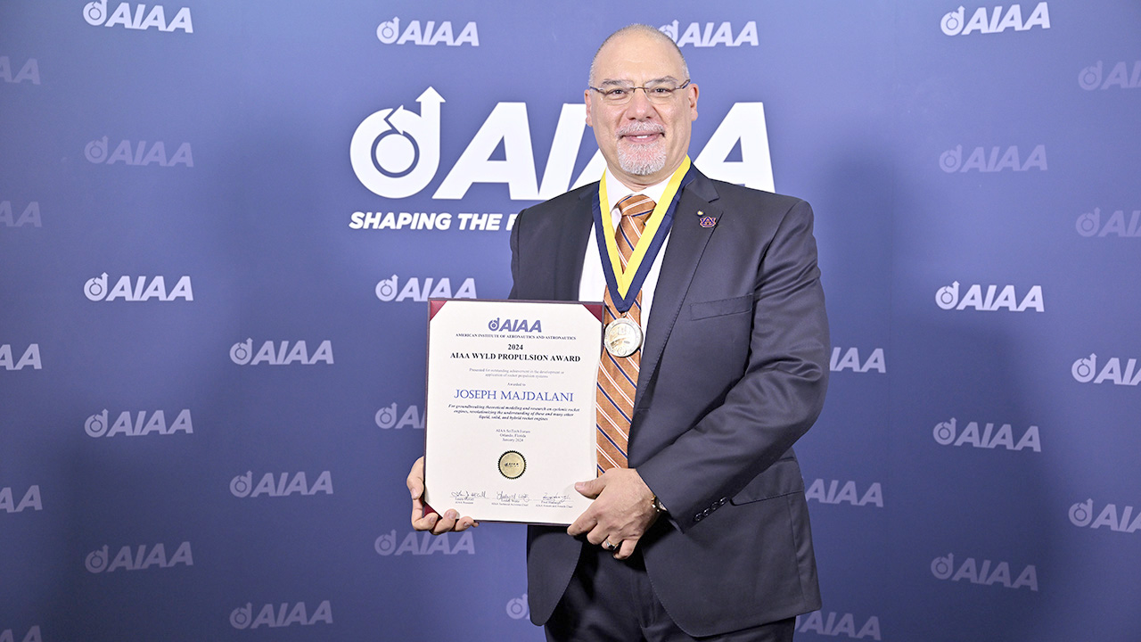  man pictured holding certificate with blue suit and blue background.