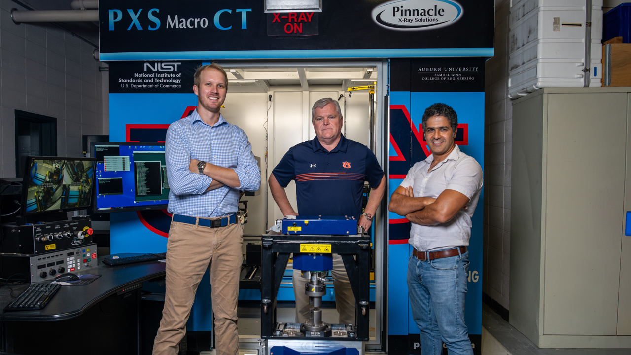 three men stand in front of a x-ray machine
