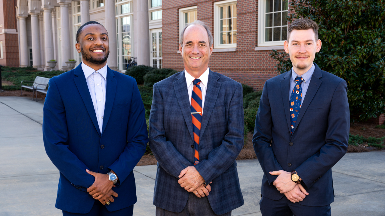 three men in blue suits pose for an outside photo