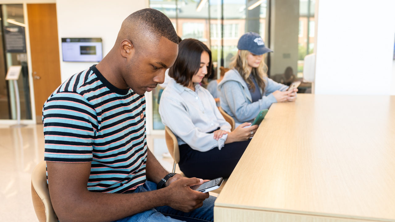 Three students look at their phones in an awkward position.