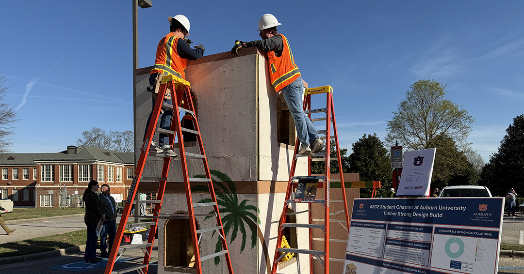  Two Auburn University students wearing safety vests and hard hats stand on ladders while working on a timber structure during an ASCE competition event.