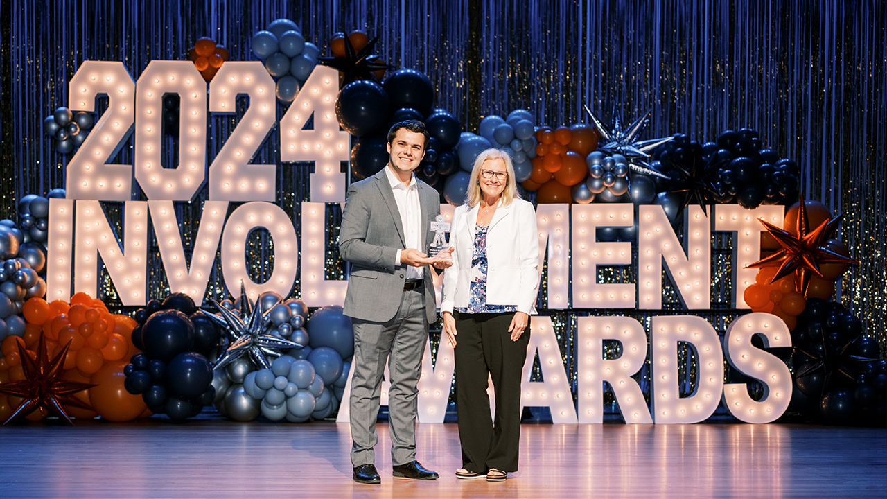 A man and a woman stand on stage to pose for a photo with an award.