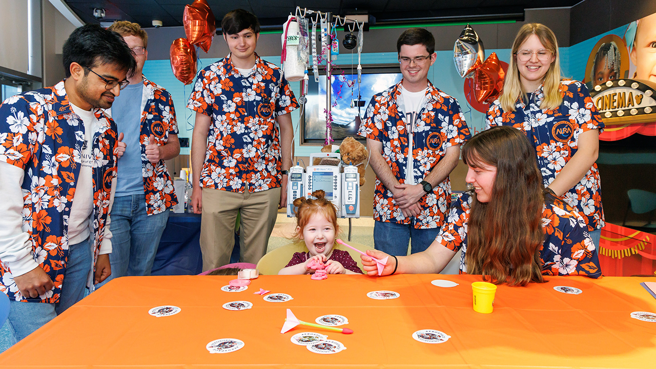 several students and a toddler stand around a table