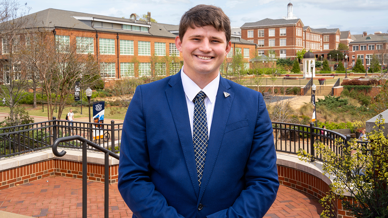 Ayden Kemp stands outside in a blue suit posing for a photo