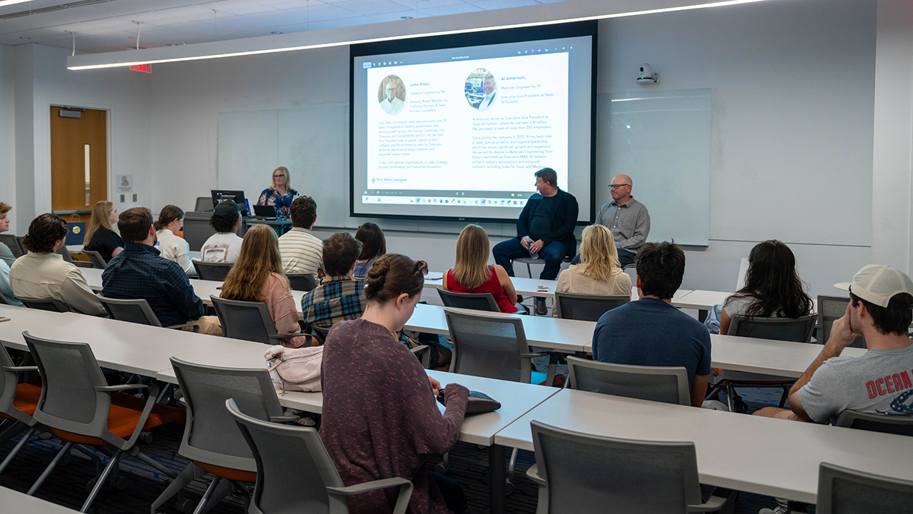  Students seated in a classroom listening to a panel of industry professionals discussing engineering career paths and experiences. 
