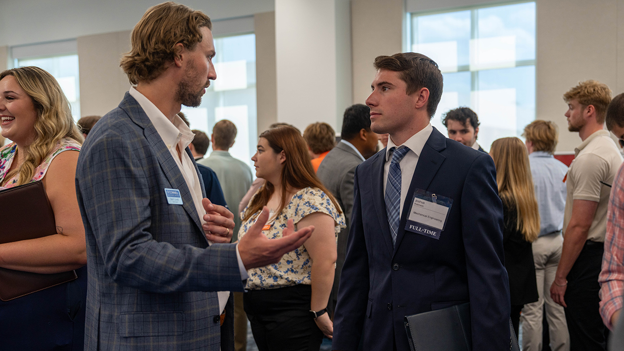 Employer representative talking with an Auburn Engineering student in a suit during a crowded career fair event.