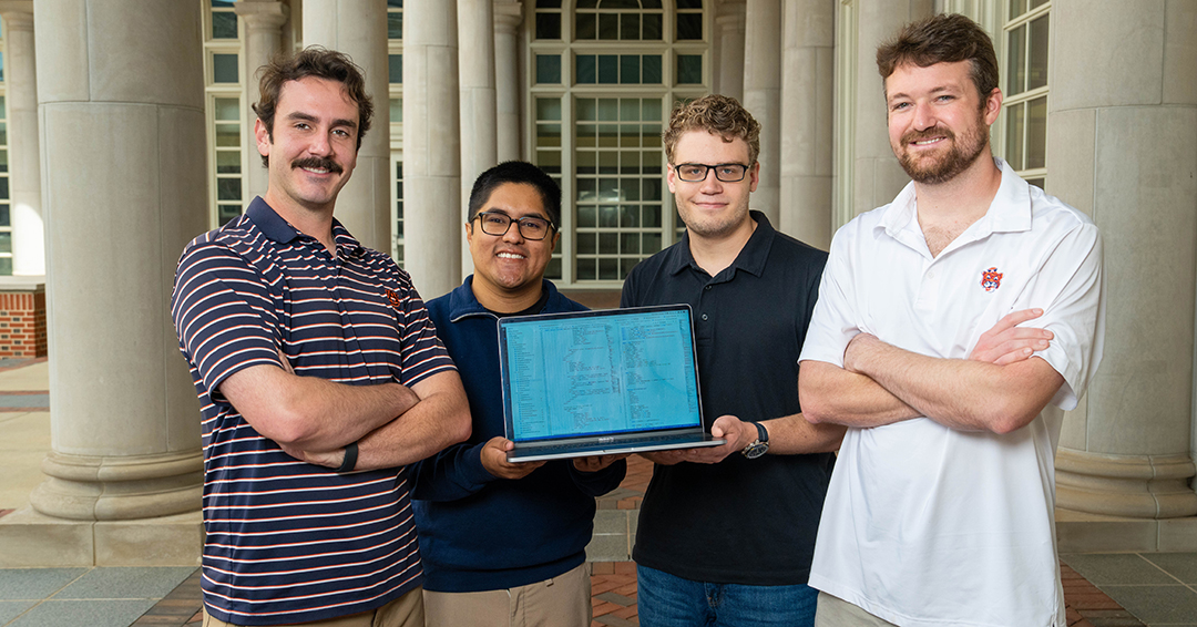 Four Auburn Engineering students stand outdoors holding a laptop displaying trajectory modeling data.
