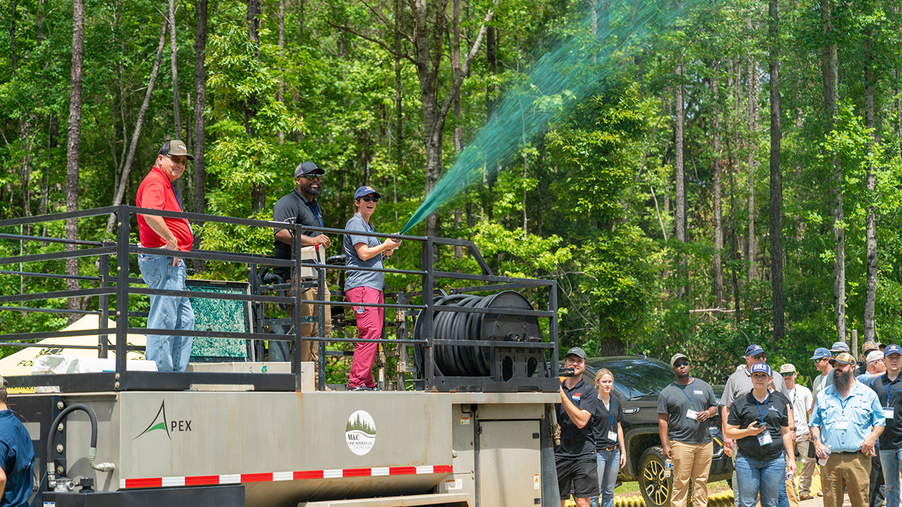  A woman with an Auburn hat on spray a green liquid from the top of a truck outside in a stormwater exercise.
