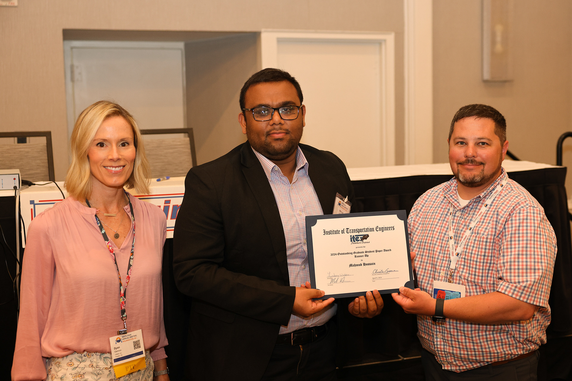 Two men and a woman pose for a photo holding an award.