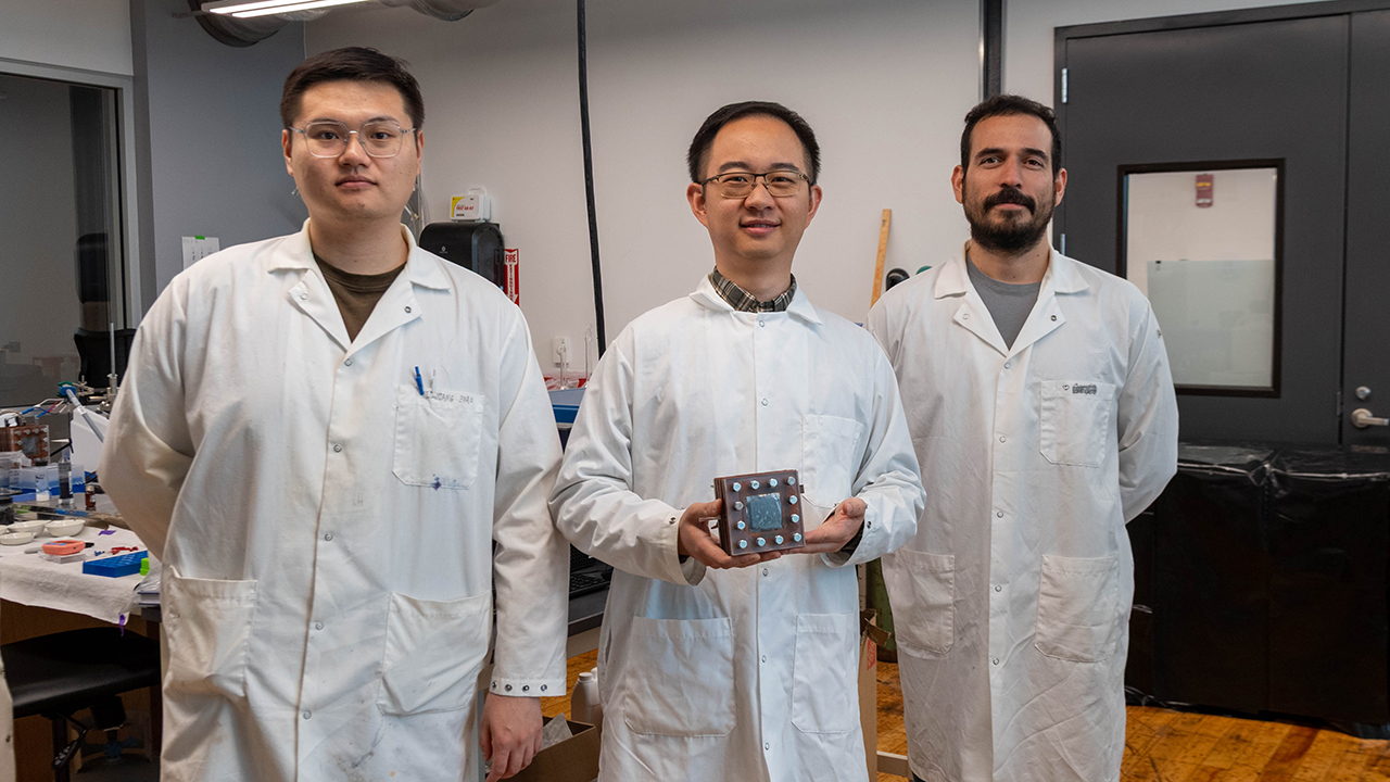 Three men poses for a photo in white lab coats in a lab