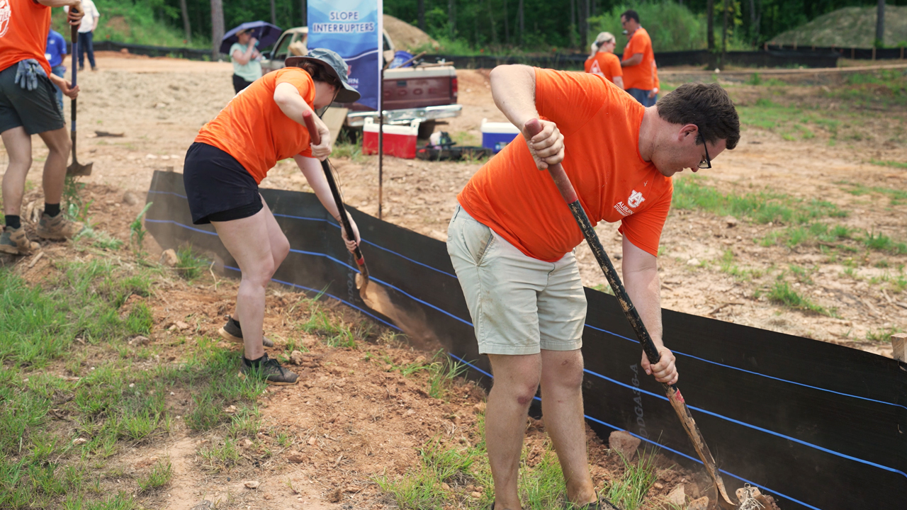 people digging trenches wearing orange shirts.