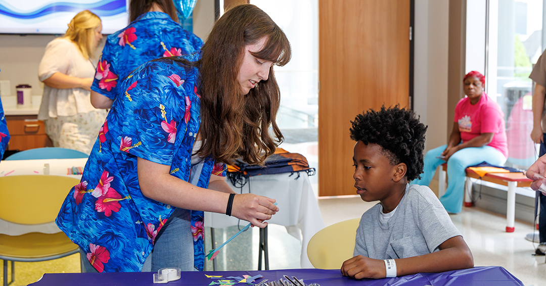  An Auburn University student helps a young patient assemble a small rocket craft at a table during a hands-on activity at Children’s of Alabama.