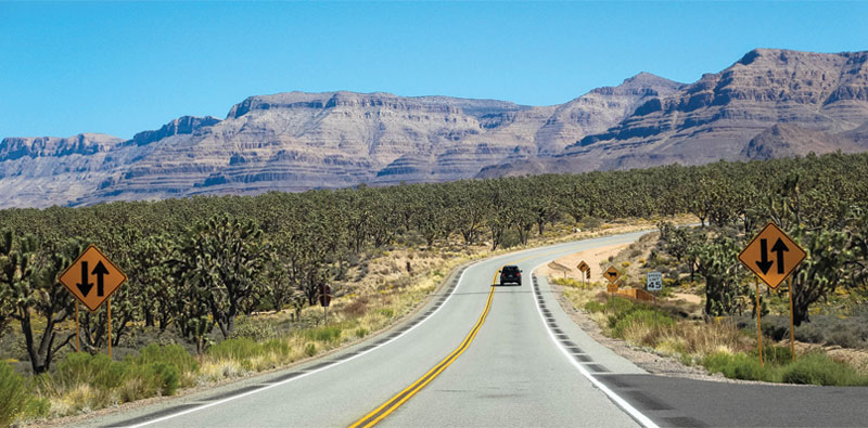 Scenic photo of car driving on desert road.